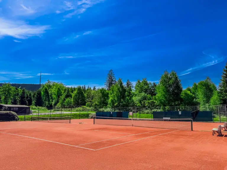 Der Tennisplatz des BLSV Sportcamp Nordbayern. Im Hintergrund steht der Sender des Ochsenkopf. Grüne Wälder und blauer Himmel im Sommer.